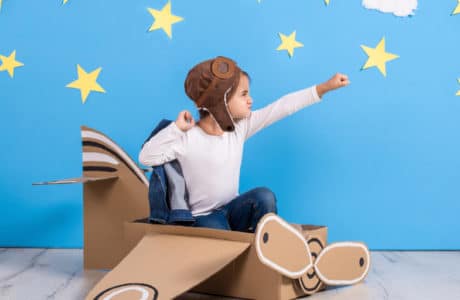 Little child girl in a pilot's costume is playing and dreaming of flying over the clouds. Portrait of funny kid on a background of bright blue wall with yellow stars and white clouds