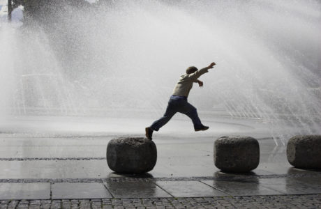Little boy jumping for joy near a water fountain.